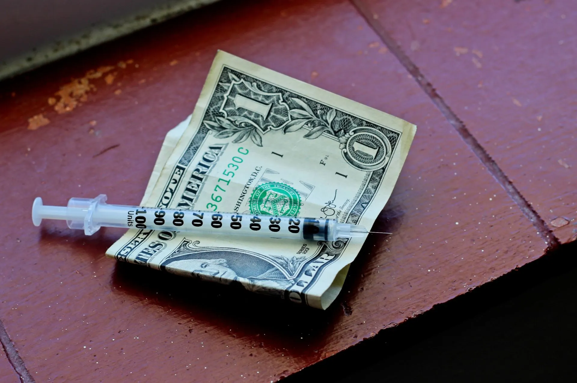 Closeup-shot-of-a-needle-on-a-one-dollar-bill-on-a-brown-surface.webp